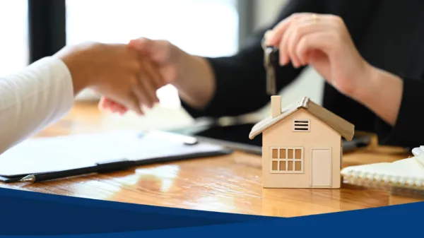 Dos personas cerrando un trato de venta de casas con apretón de manos y la entrega de llaves. Modelo de casa en primer plano.